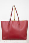 A red pebbled leather tote bag with dark red handles and gold-tone hardware, displayed on a white marble block against a white background.