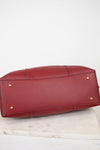 A red pebbled leather handbag shown from the bottom, resting on a white marble surface against a white background.