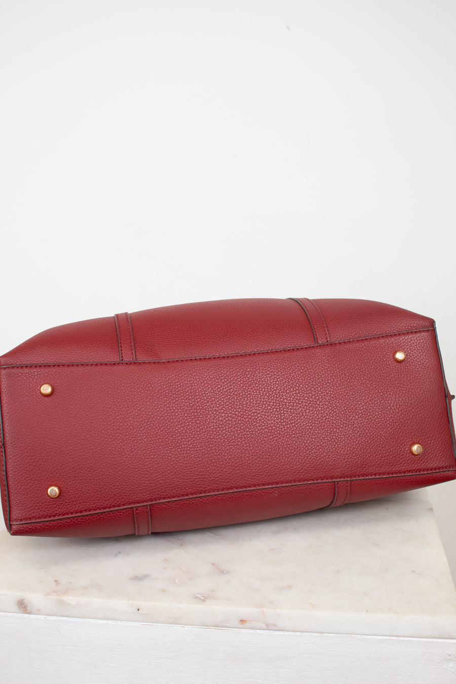 A red pebbled leather handbag shown from the bottom, resting on a white marble surface against a white background.