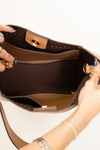 Brown handbag with gold accents held by a person on a white background