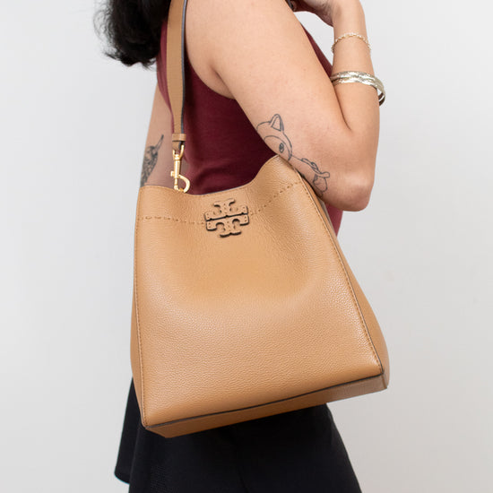 Person holding a tan handbag with a visible brand logo against a plain background