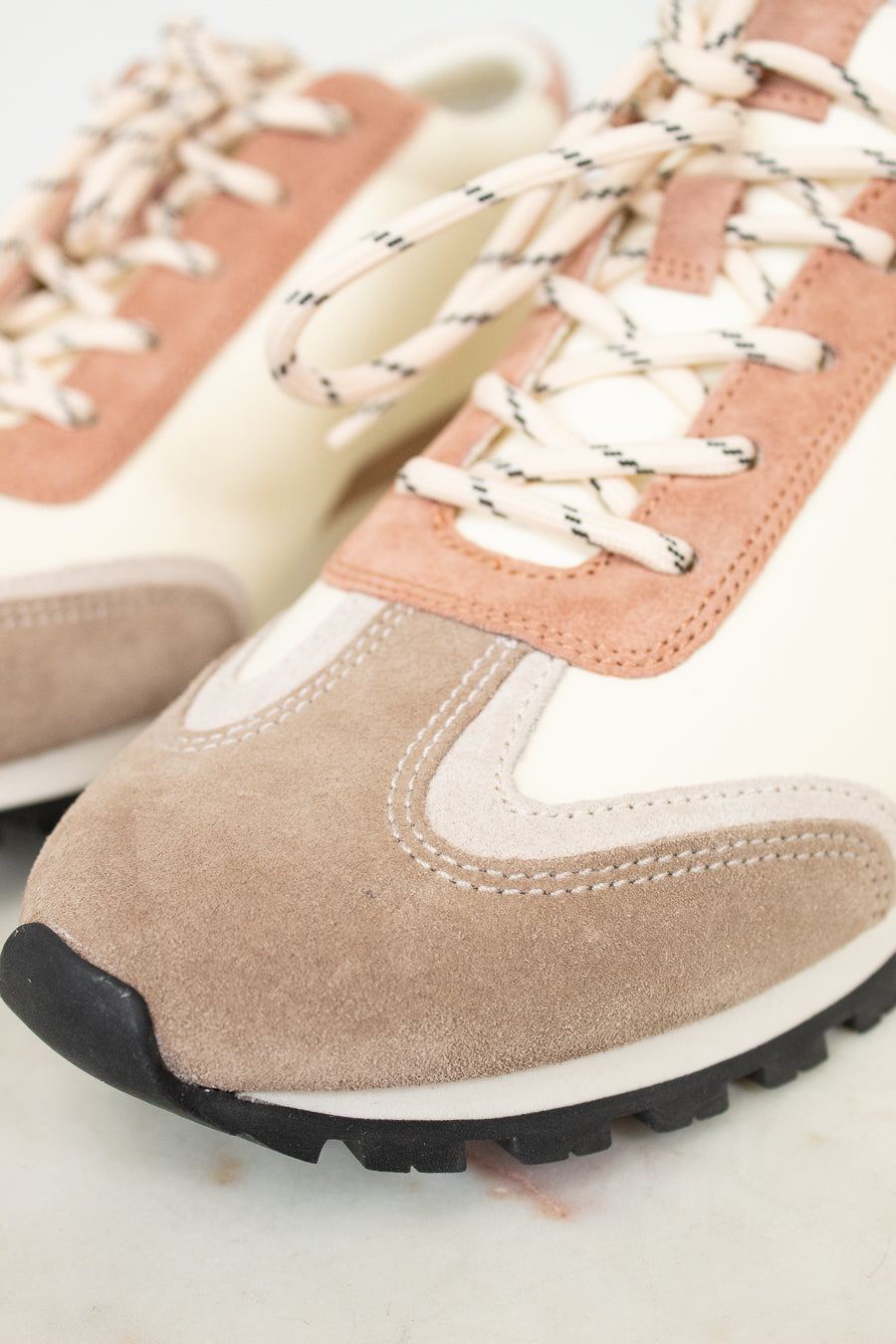 Close-up of a pair of sneakers with pink and beige accents on a light background