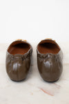 A pair of women's brown leather ballet flats with gathered detailing and gold-tone hardware, shown from the back on a light marble surface.