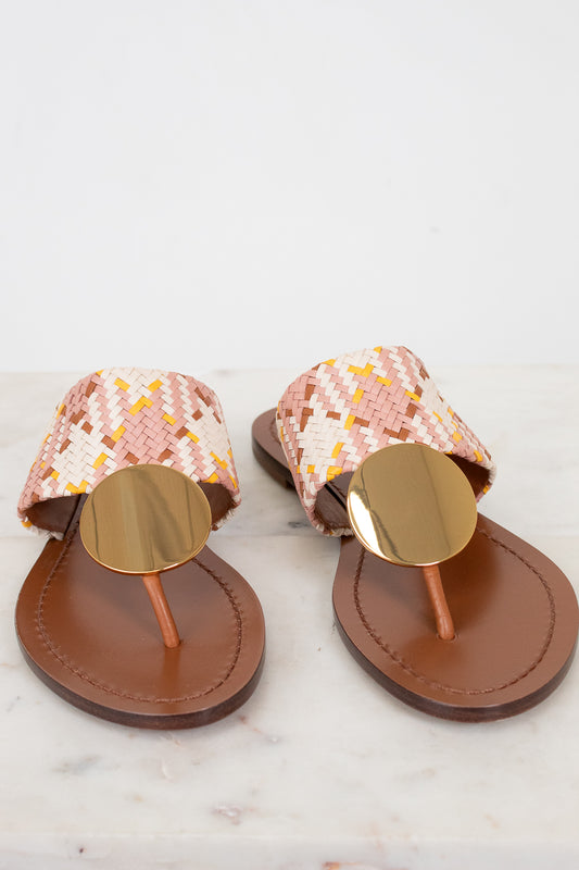 Pair of sandals with woven straps and round gold buckle detail on a white background