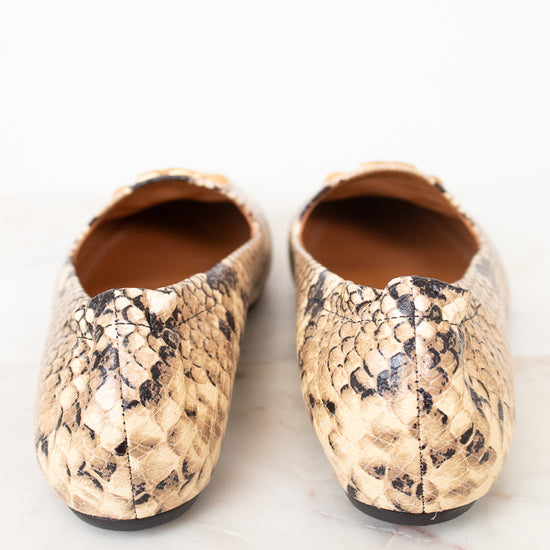 A pair of women's ballet flats featuring a beige and black python skin pattern, photographed from a top-down angle on a light marble surface.