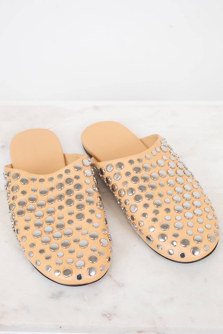 Pair of beige slippers with silver stud details on a light background