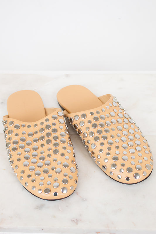 Pair of beige slippers with silver stud details on a light background