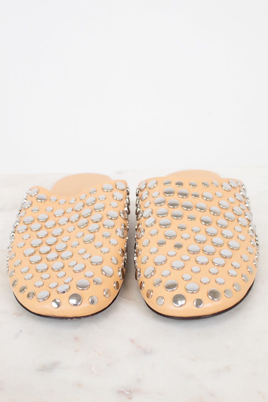 Pair of beige slippers with silver studs on a white background
