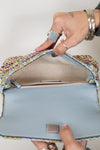 Hand holding open woven handbag with , showing its light blue lining and tan interior.