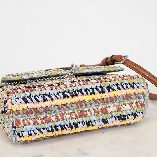 Multicolored woven handbag with a brown strap on a light wooden surface.