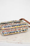 Multicolored woven handbag with a brown strap on a light wooden surface.