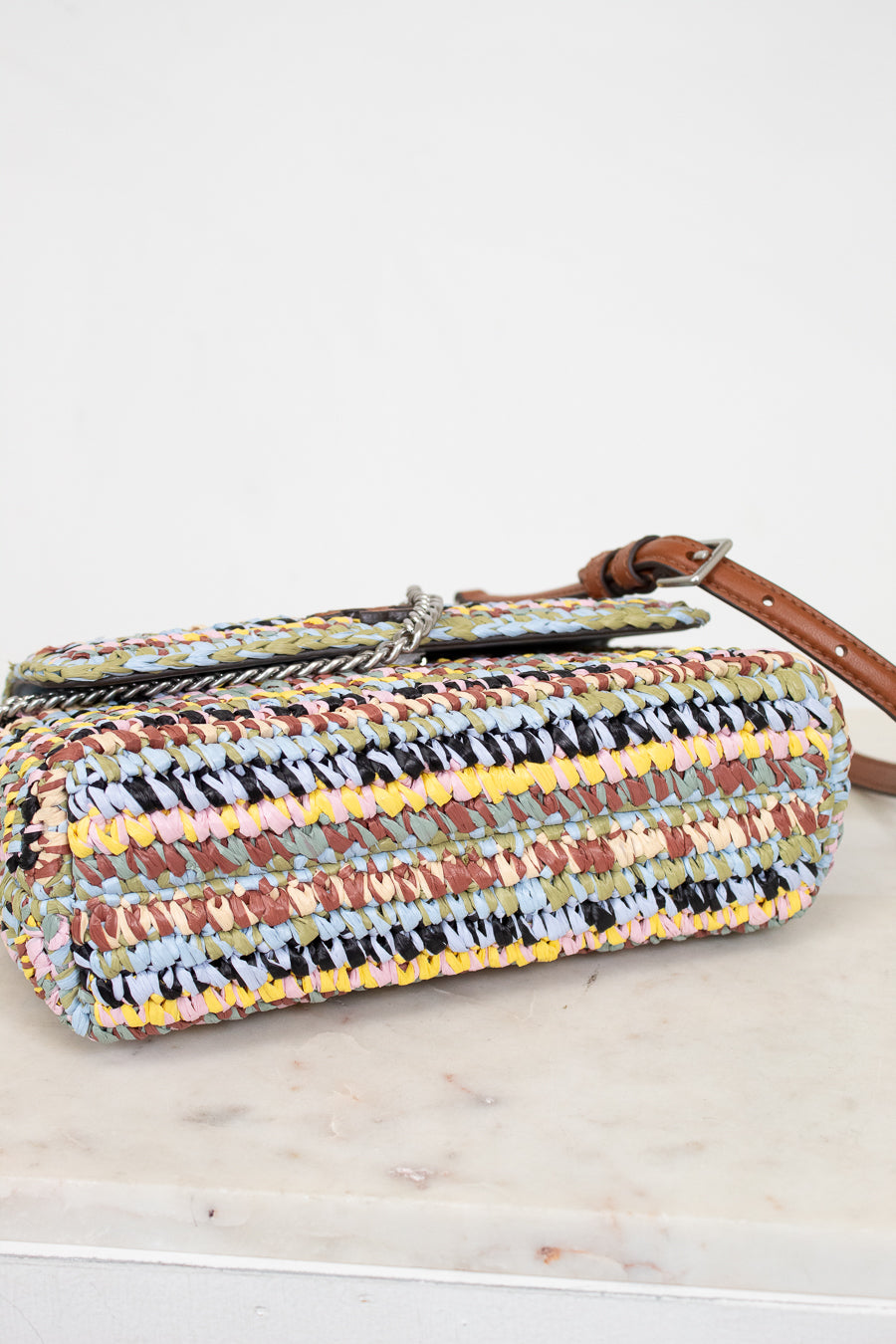 Multicolored woven handbag with a brown strap on a light wooden surface.