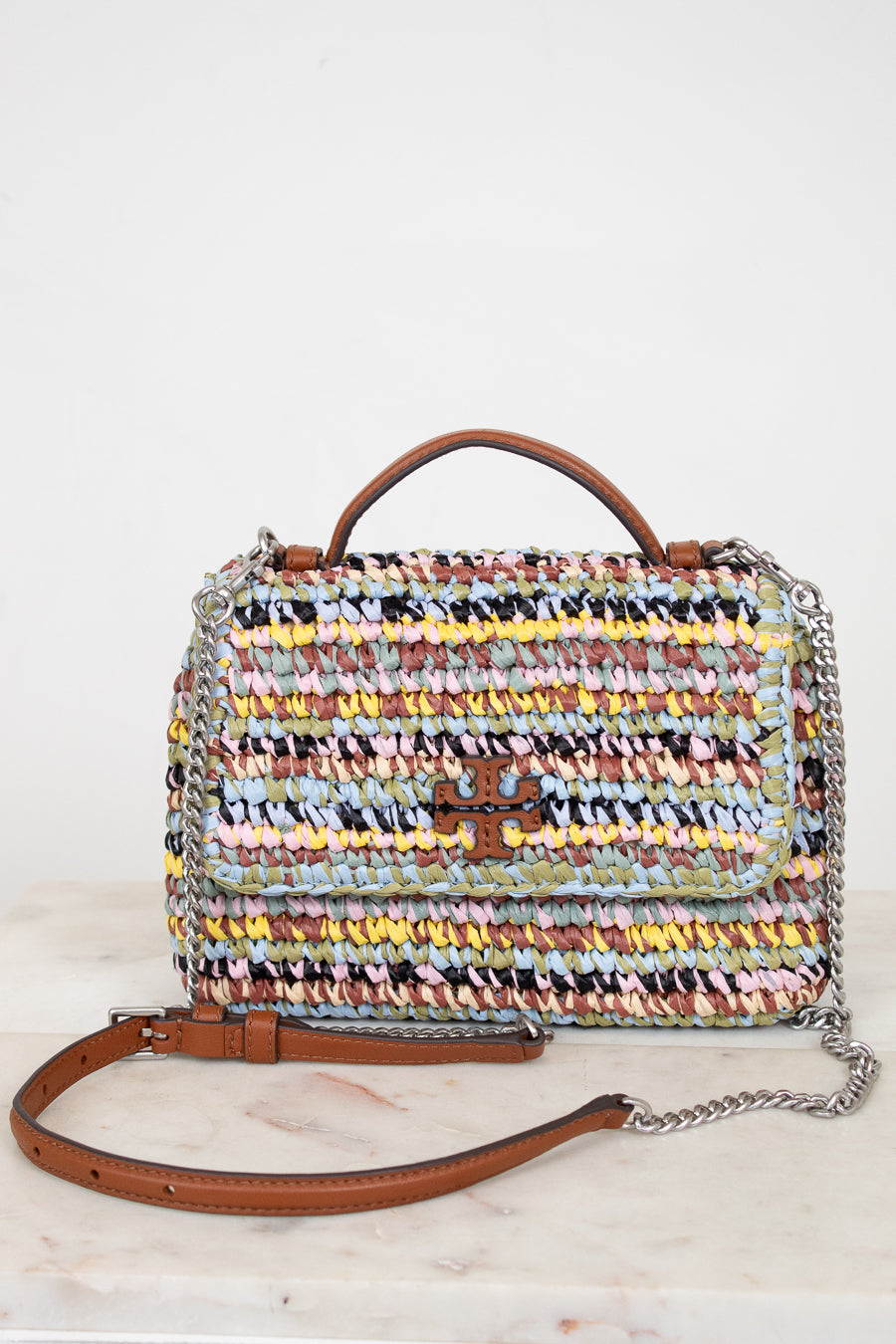 Multicolored woven handbag with a chain detail on a white background