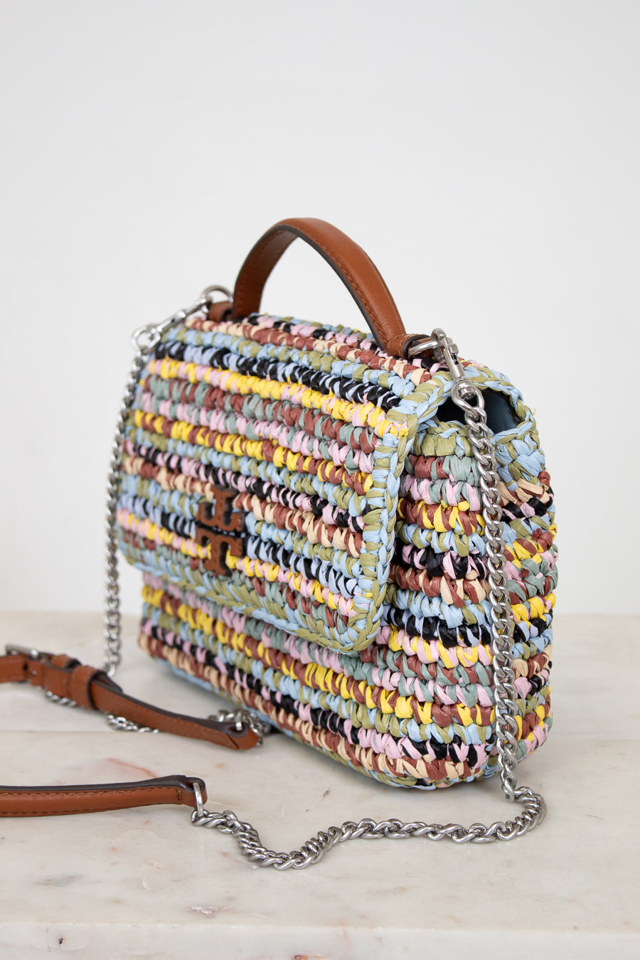 Multicolored woven handbag with a brown Tory Burch logo and chain detail on a light background