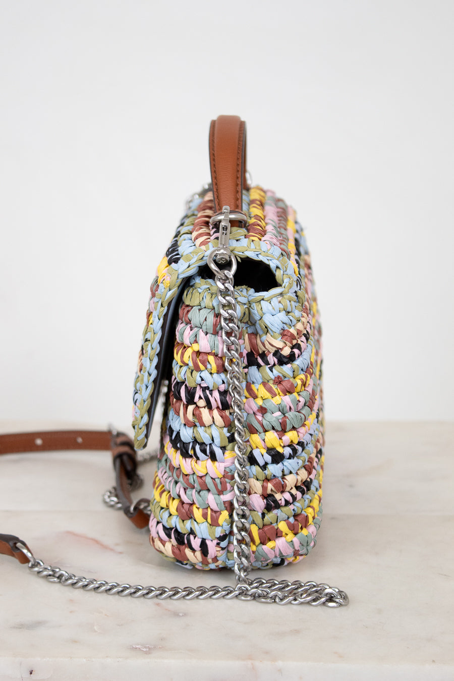 Multicolored woven handbag with a chain detail on a white background
