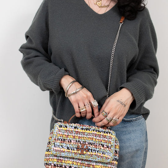 Person holding a multicolored woven handbag against a plain background