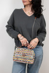 Person holding a multicolored woven handbag against a plain background