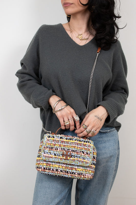 Person holding a multicolored woven handbag against a plain background