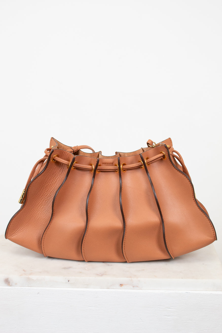 Tan leather handbag with drawstring on a white background