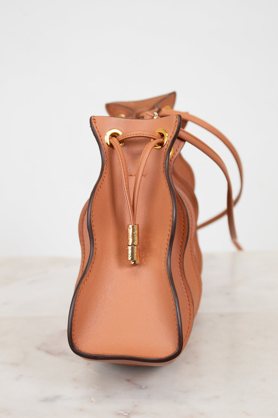 Tan leather side profile of bag with drawstring on a light marble background