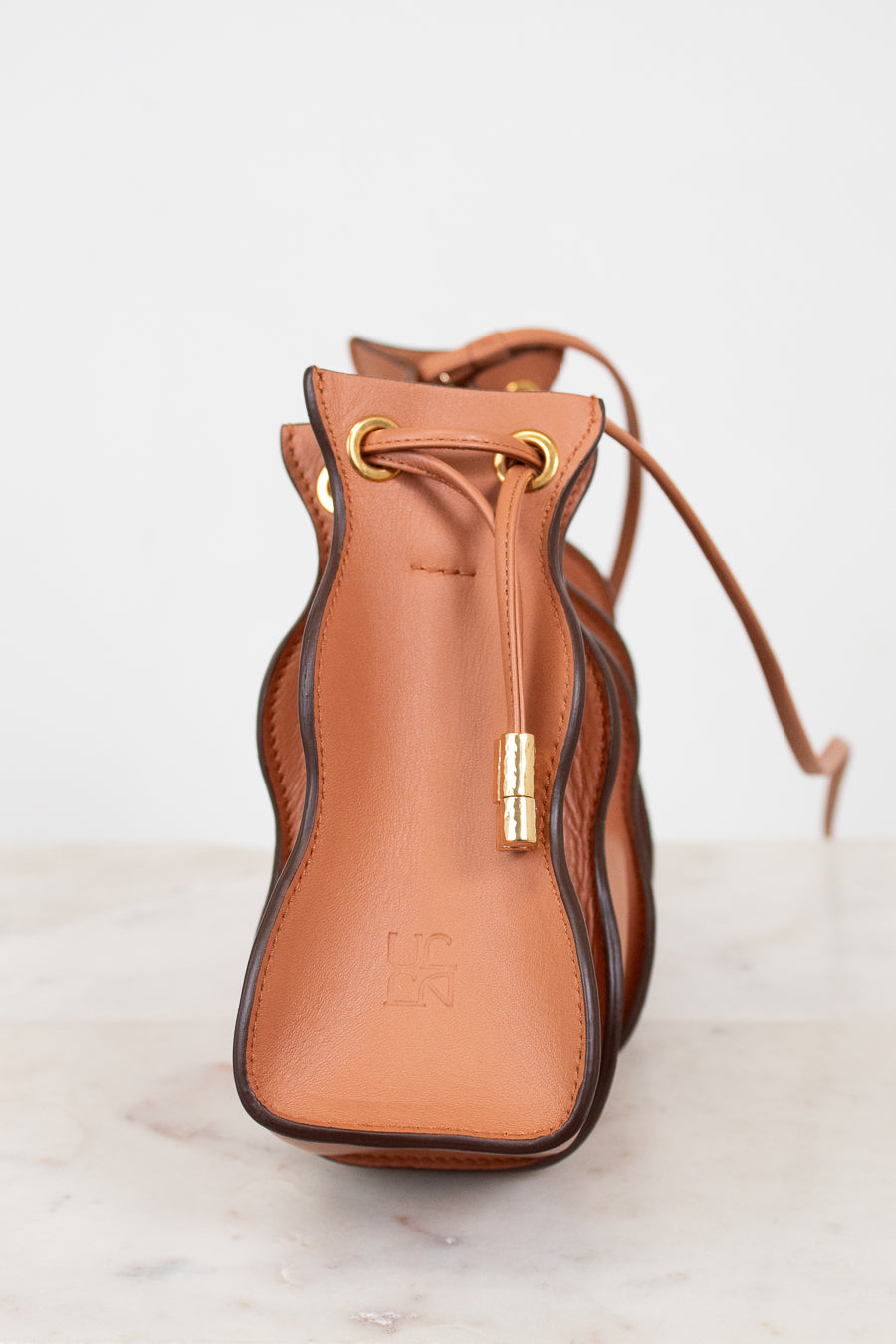 Brown leather drawstring bag with gold accents on a light background