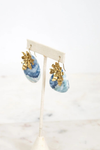Pair of earrings with blue and gold design on a white stand against a light background