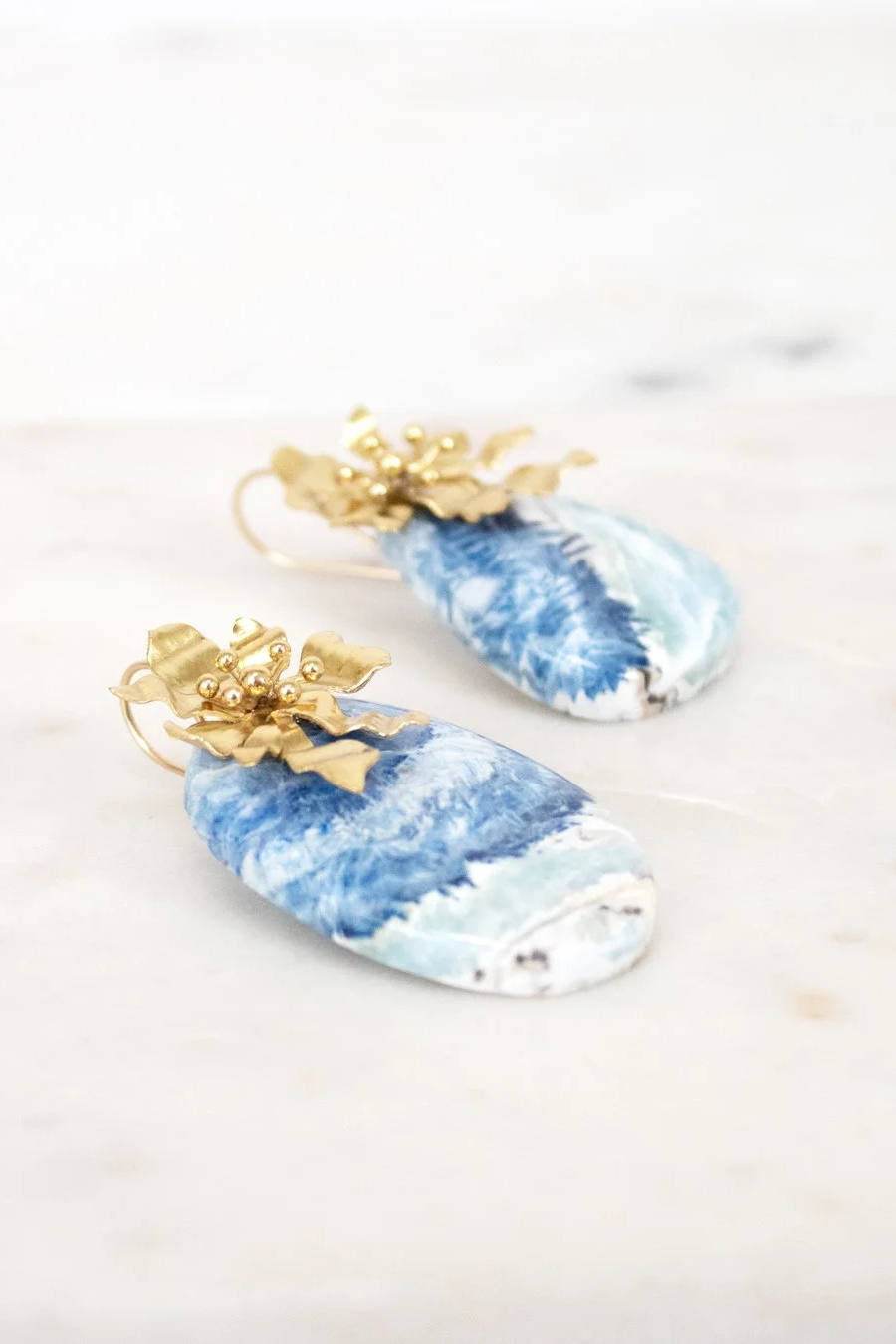 Blue and white marbled earrings with gold accents on a light background