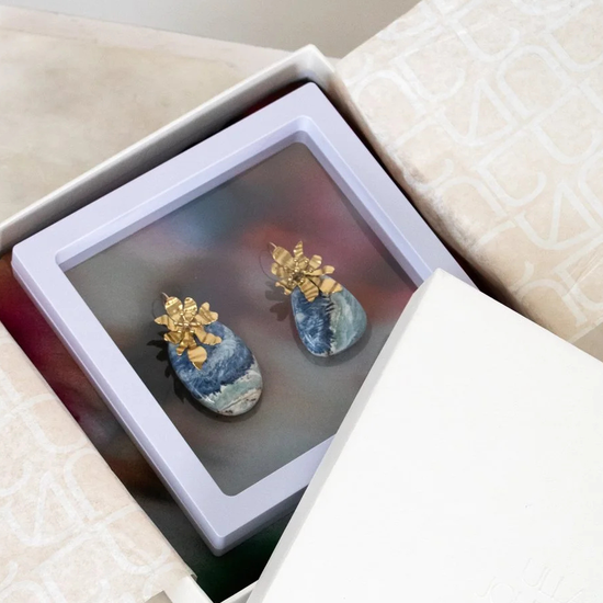Pair of blue and gold earrings in a jewelry box on a light surface.