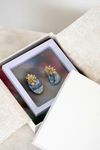 Pair of blue and gold earrings in a jewelry box on a light surface.