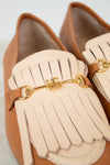 Pair of tan loafers with beige tassels and gold accents on a light gray background