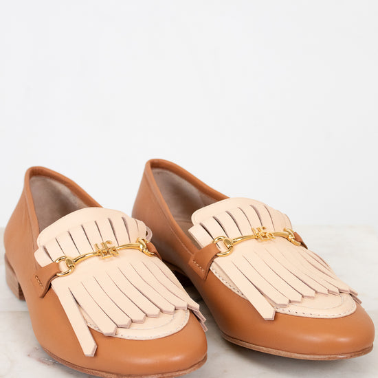 Pair of tan and beige loafers with tassel details on a light background
