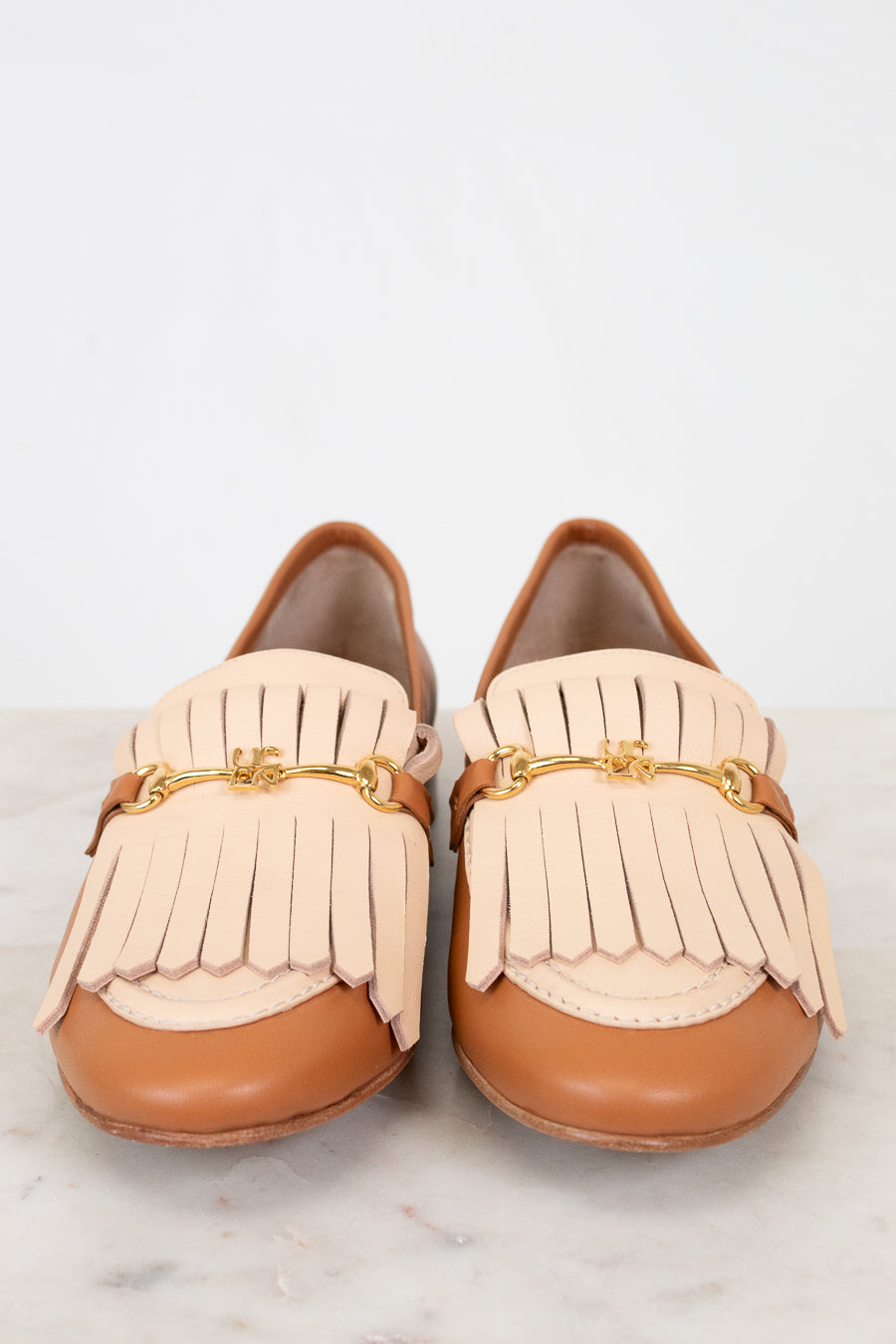 Pair of tan loafers with beige fringe on a light background