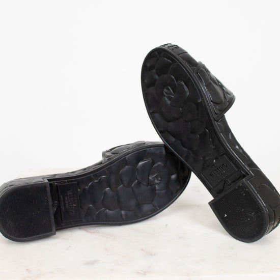 Black sandals with floral details and a Valentino brand logo on a white background