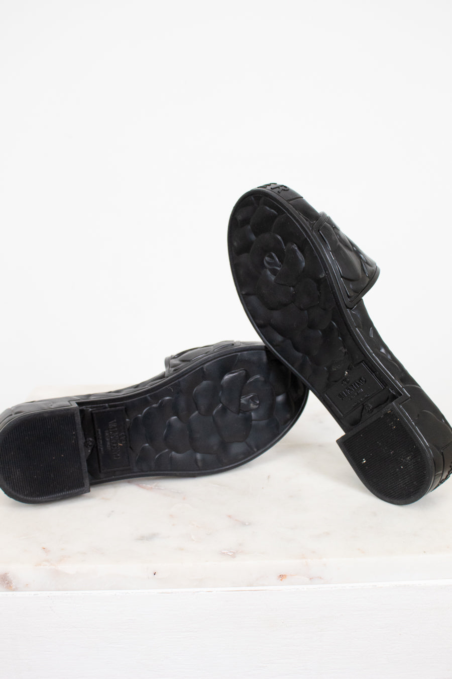 Black sandals with floral details and a Valentino brand logo on a white background