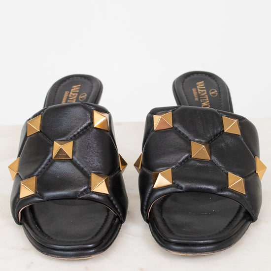 A pair of black leather slide sandals featuring gold pyramid studs and a quilted pattern, with the brand name Valentino visible on the insole.