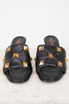 A pair of black leather slide sandals featuring gold pyramid studs and a quilted pattern, with the brand name Valentino visible on the insole.