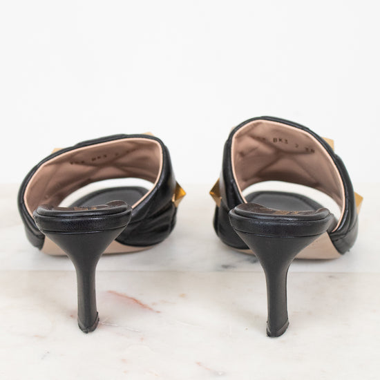 A pair of black leather slingback kitten heels with gold-tone hardware, shown from the back on a white marble surface against a white background.