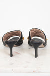 A pair of black leather slingback kitten heels with gold-tone hardware, shown from the back on a white marble surface against a white background.