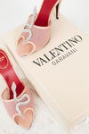 Pink high-heeled shoes with decorative elements on a Valentino Garavani box.