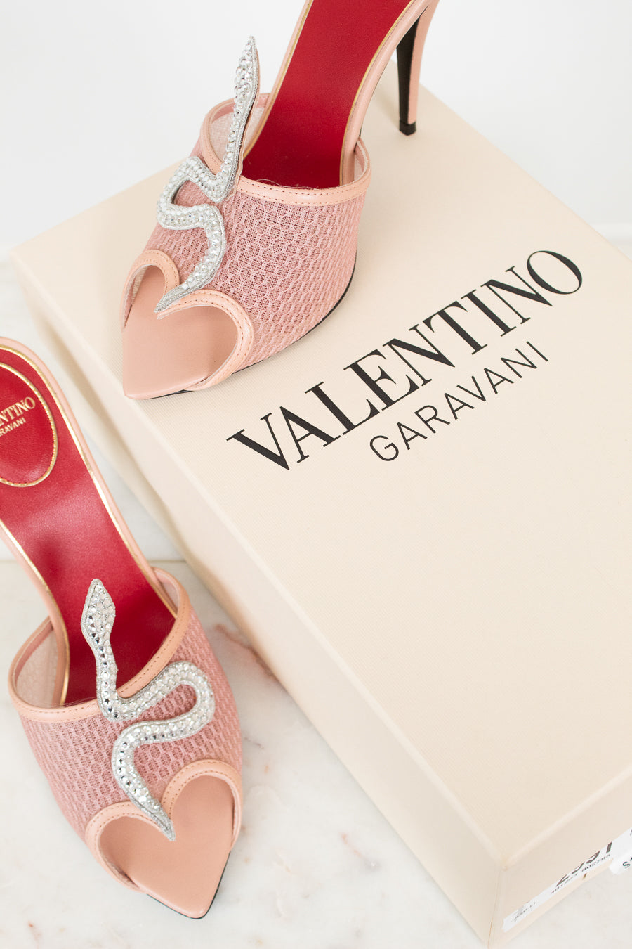 Pink high-heeled shoes with decorative elements on a Valentino Garavani box.