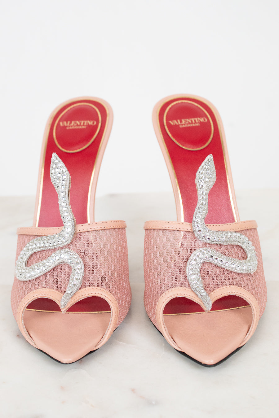 Pink high-heeled shoes with decorative elements on a light gray background