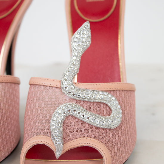 Pink high-heeled shoes with silver snake design on a light background