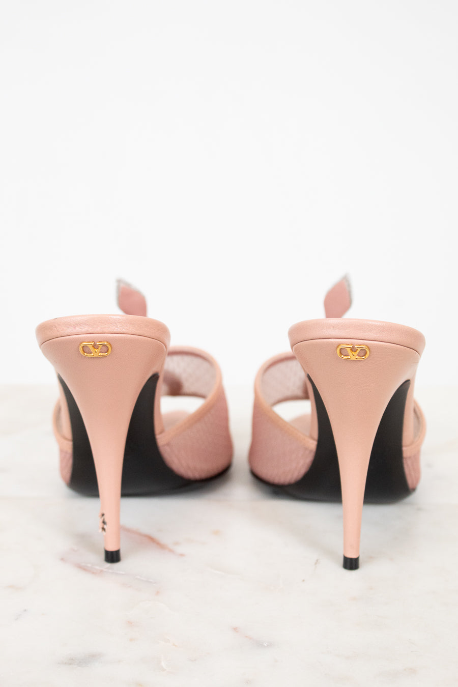 Pair of pink high-heeled shoes with black soles on a white background