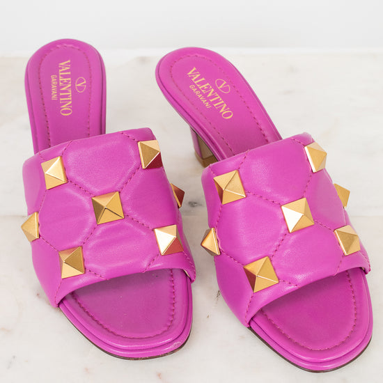 Pink heeled sandals with gold studs on a white background