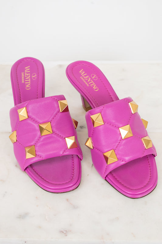 Pink heeled sandals with gold studs on a white background