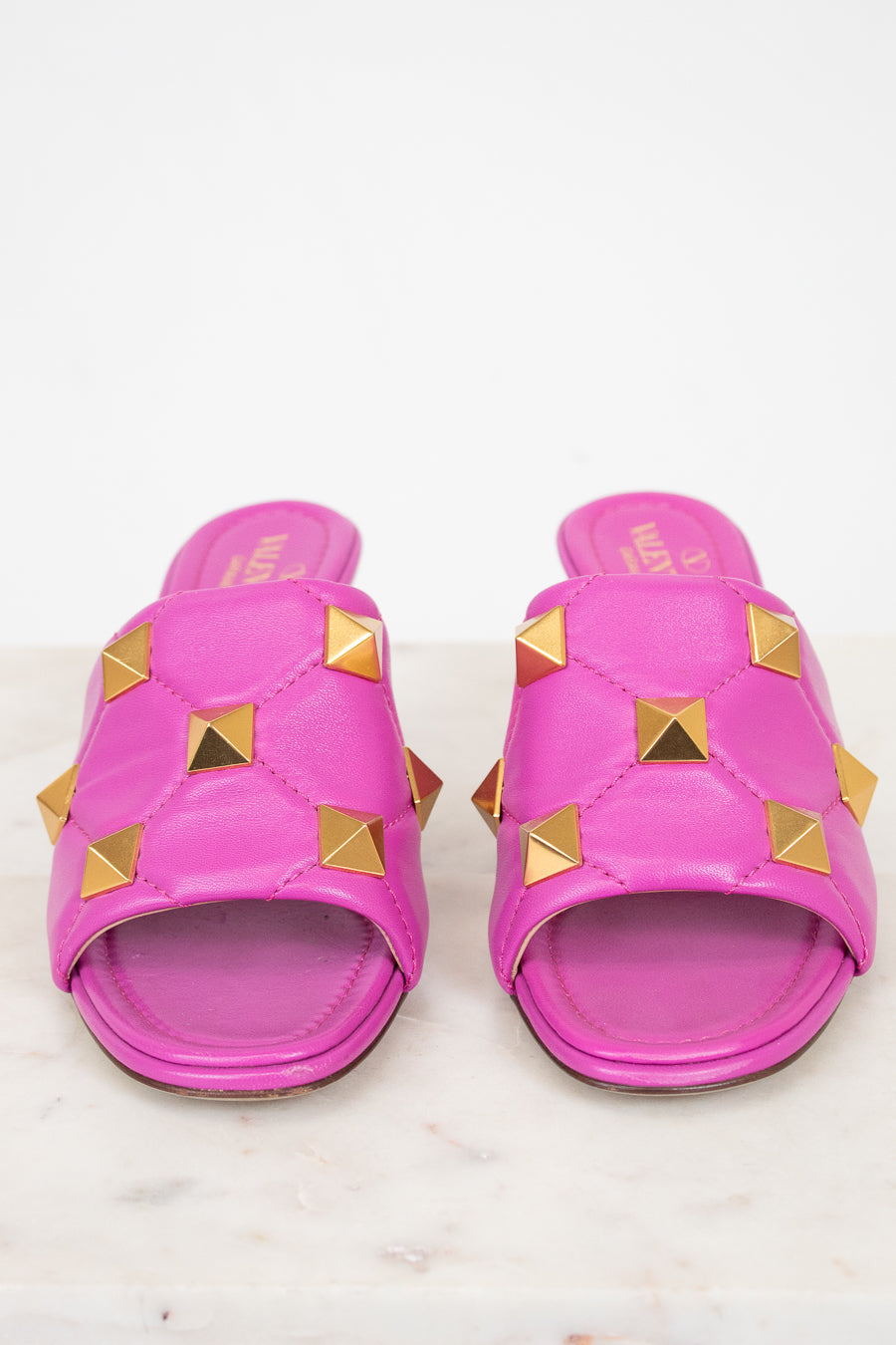 Pair of pink heeled sandals with gold studs on a white background