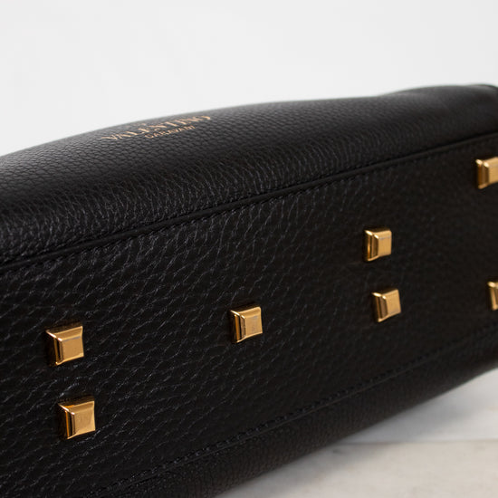 Black handbag with gold studs on a light gray background