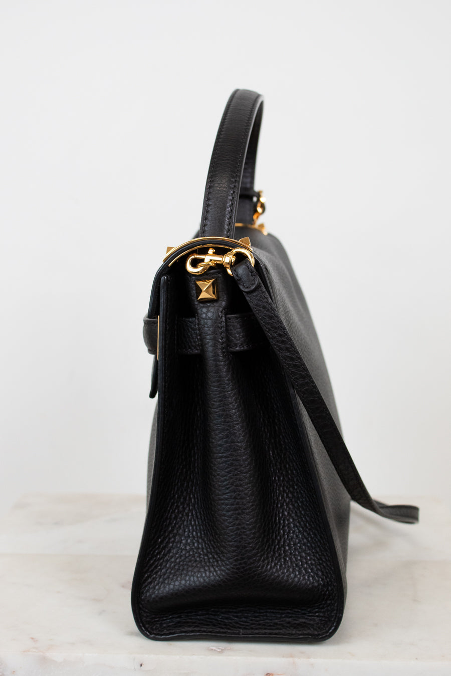 Black leather handbag with gold hardware on a white background