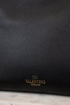 Black leather handbag with 'Valentino Garavani' logo on a marble surface