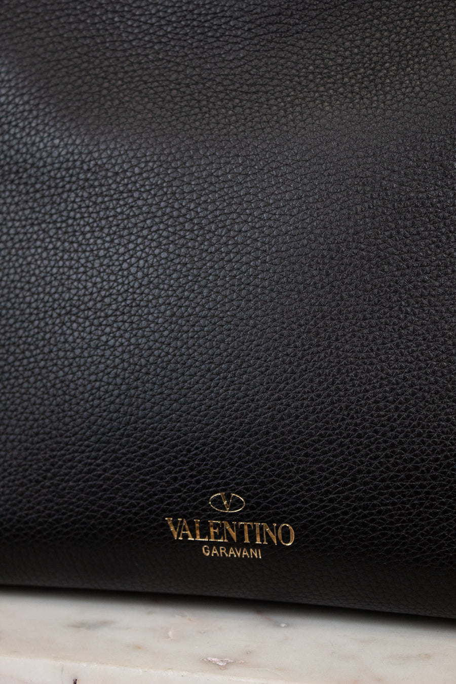 Black leather handbag with 'Valentino Garavani' logo on a marble surface